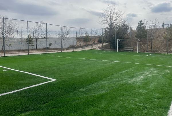 Tel çitle çevrili sentetik çim futbol sahası ve kale