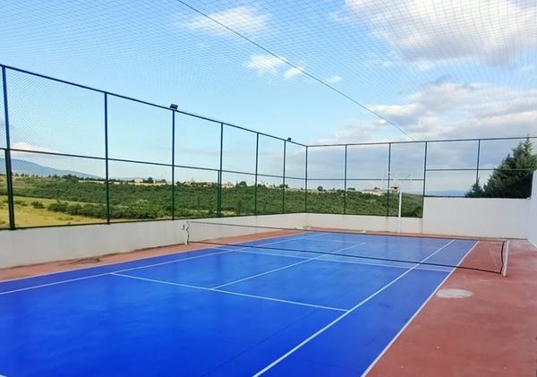Yeşil yamaçlara bakan mavi zeminli açık spor sahası