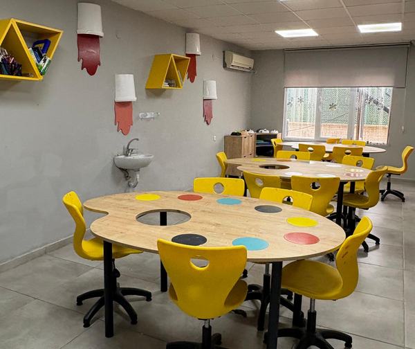 Palet biçimli masaları ve sarı sandalyeleriyle resim atölyesi