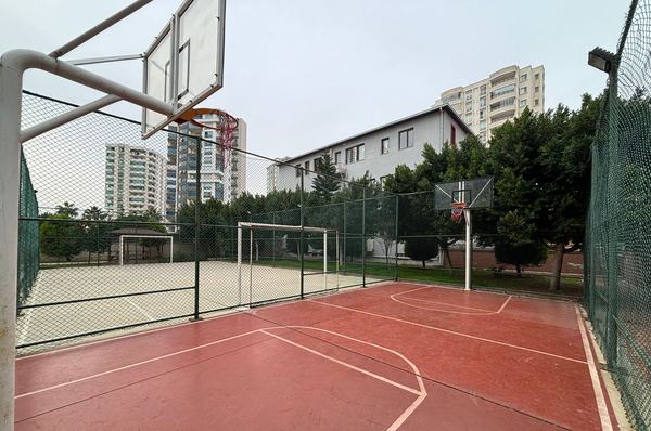 Çitle çevrili basketbol sahası, futbol sahası ve okul binası