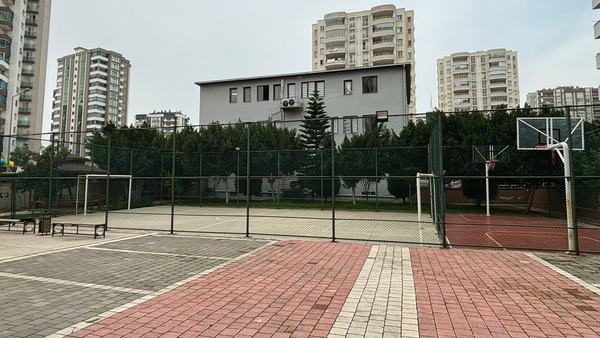 Taş döşeli avlu, çitli spor sahaları ve okul binası